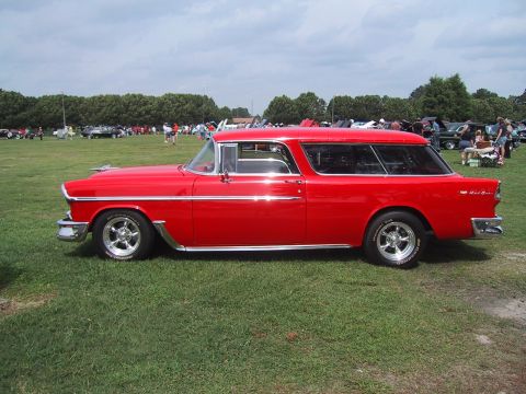 1968 Shelby GT500 - A red 1955 Chevrolet Nomad station wagon is displayed at a car show with other vehicles in the background.