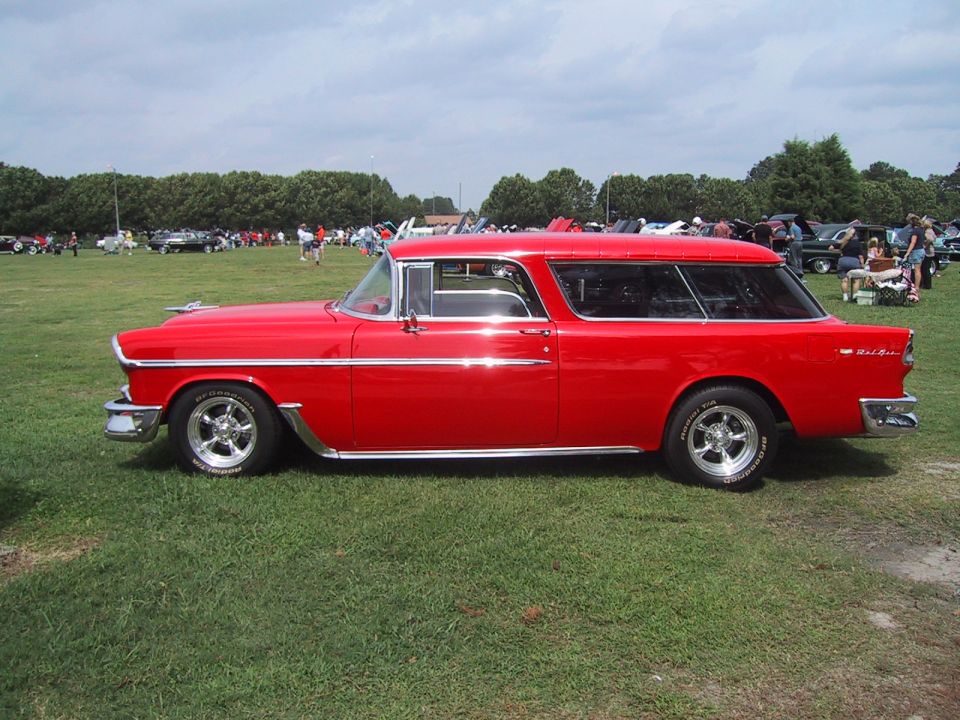 Red 1955 Chevrolet Nomad station wagon parked on grass at a car show