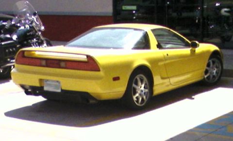 1988 Pontiac Fiero - Rear view of a yellow Acura NSX sports car parked outdoors next to a motorcycle.