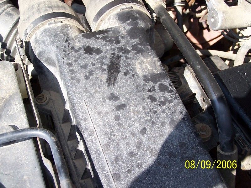 Close-up of a dirty engine air intake housing with oil stains. Date stamp reads 08/09/2006