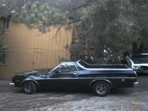 1973 Ford Ranchero - A black Ford Ranchero is parked in front of a yellow building with trees overhead.