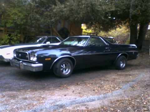 1973 Ford Ranchero - A black 1973 Ford Ranchero is parked next to another vehicle under trees.