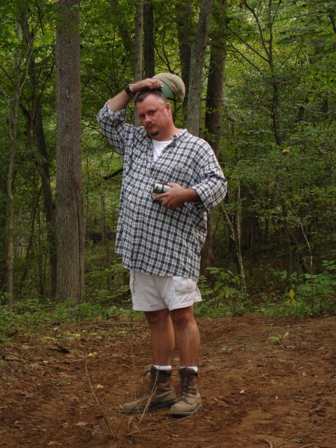 1996 Ford Bronco - A man stands in a wooded area, holding a hat on his head and a camera in his hand.