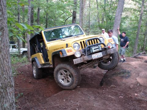 1996 Ford Bronco - A yellow Jeep Wrangler Rubicon navigates a rocky off-road trail with spectators nearby.