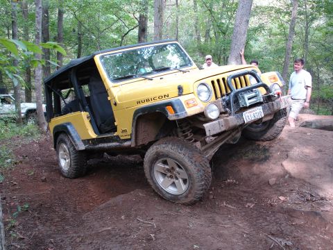 1996 Ford Bronco - A yellow Jeep Wrangler Rubicon navigates an off-road trail, with another white vehicle visible in the background.