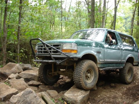 1996 Ford Bronco - A two-tone green Ford Bronco is shown tackling a rocky off-road trail.