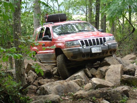 1996 Ford Bronco - A red Jeep Grand Cherokee navigates a rocky trail, with a spare tire mounted on the roof.