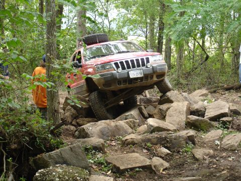1996 Ford Bronco - A red Jeep Grand Cherokee tackles a challenging rock crawling course, demonstrating its off-road capabilities.