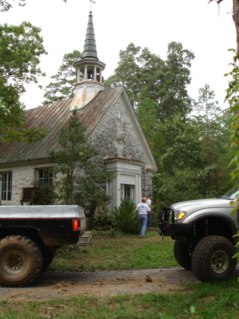 1996 Ford Bronco - Two modified trucks are parked near an old stone building with a steeple.