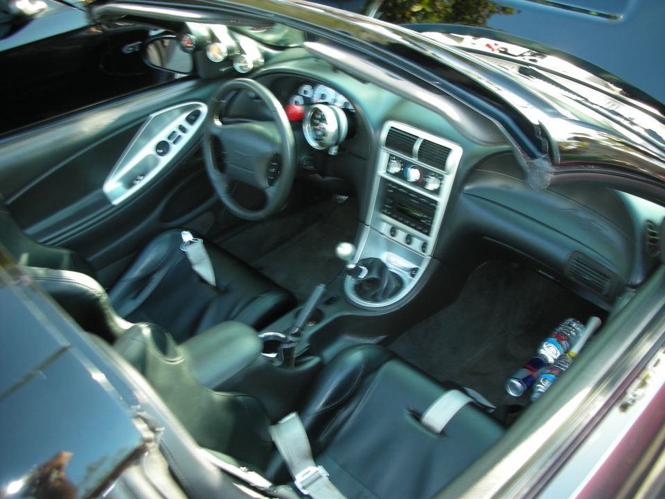 Car interior with racing seats, aftermarket gauges, and a manual shifter. Drinks are on the floor