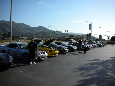 1992 Ford Crown Victoria - A group of cars are parked in a lot under a clear blue sky with mountains in the distance.