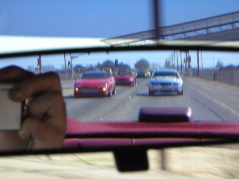 1992 Ford Crown Victoria - A hand holds a card in front of the rearview mirror, obscuring part of the view of cars on the road.