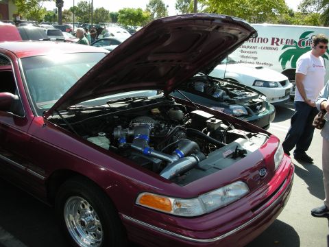 1992 Ford Crown Victoria - A maroon 1992 Ford Crown Victoria is displayed with its hood open, revealing a modified engine with twin turbochargers.