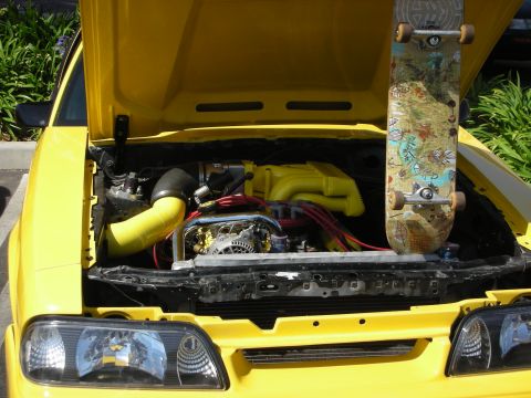 1992 Ford Crown Victoria - A skateboard rests against the engine of a yellow car, with the hood open.