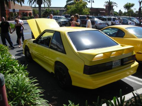 1992 Ford Crown Victoria - A yellow coupe with its hood up is parked next to another yellow vehicle in a parking lot.