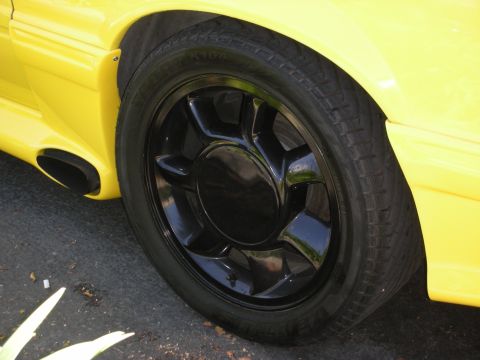 1992 Ford Crown Victoria - A close-up view of a yellow car's rear wheel and exhaust system, black aftermarket wheels.