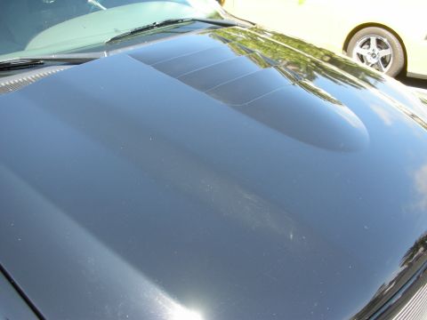 1992 Ford Crown Victoria - Close-up of a black car's hood a set of three distinct vents, with another vehicle partially visible in the background.