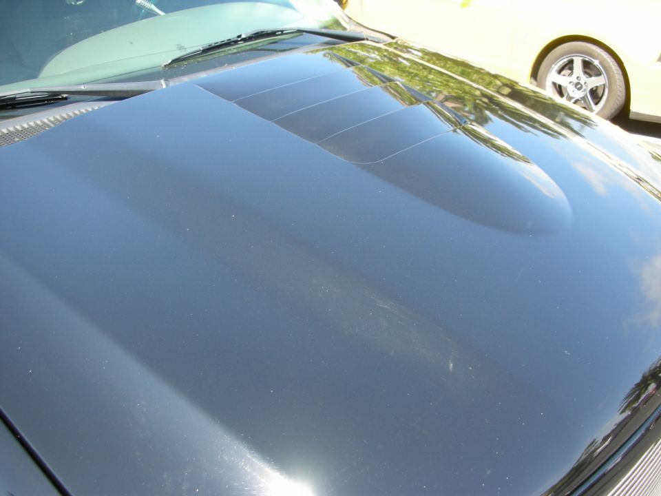 Black car hood with triple vents. Yellow car visible in background