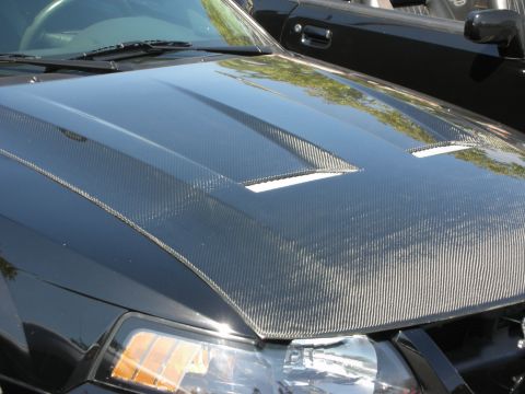 1992 Ford Crown Victoria - Close-up of a black car's hood a carbon fiber finish and dual vents, with another vehicle visible in the background.