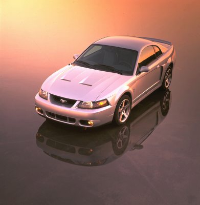2003 Ford Mustang - A silver 2003 Ford Mustang is shown from a high angle, reflecting on a dark, glossy surface under a warm-toned sky.