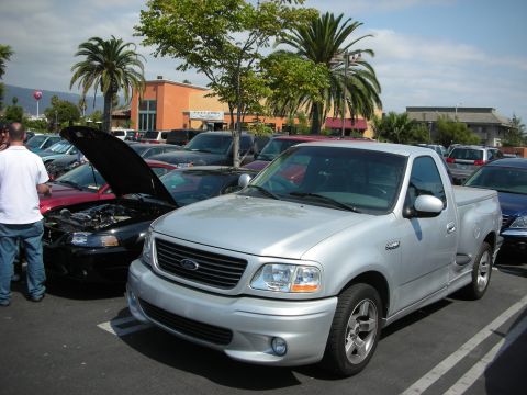 1992 Ford Crown Victoria - A silver Ford F-150 Lightning pickup truck is parked in a lot, with a black Mustang and other vehicles nearby.