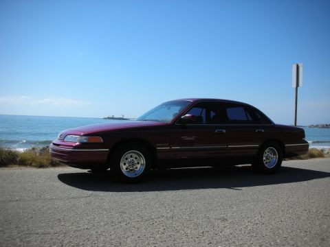 1992 Ford Crown Victoria - A maroon 1992 Ford Crown Victoria is parked on the side of the road with the ocean in the background.