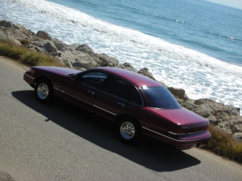1992 Ford Crown Victoria - A maroon 1992 Ford Crown Victoria is parked on a coastal road with waves crashing on the rocks.