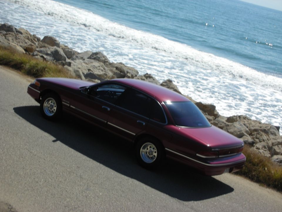 Maroon 1992 Ford Crown Victoria parked on a road next to the ocean