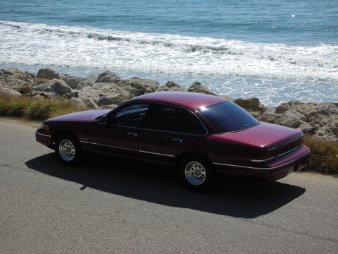 1992 Ford Crown Victoria - A maroon 1992 Ford Crown Victoria sedan is parked on a road next to a rocky coastline and the ocean.