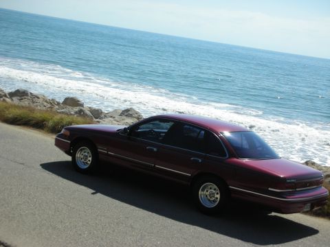 1992 Ford Crown Victoria - A maroon 1992 Ford Crown Victoria is parked on a road overlooking the ocean.