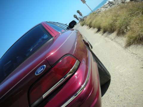 1992 Ford Crown Victoria - The rear of a maroon Ford Crown Victoria is seen from a low angle, parked on a dirt road with the ocean in the background.
