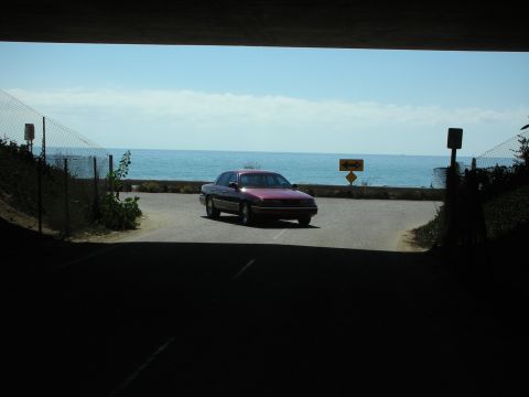 1992 Ford Crown Victoria - A maroon sedan drives on a road with the ocean in the background.