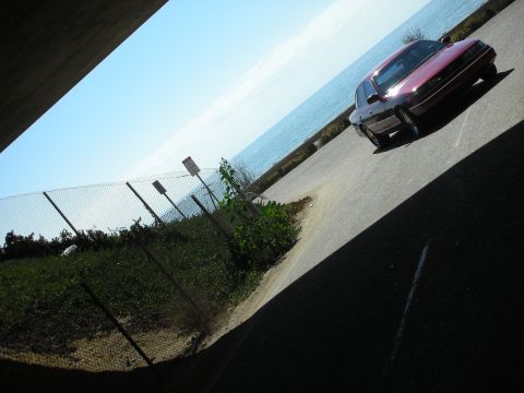 1992 Ford Crown Victoria - A maroon 1992 Ford Crown Victoria is seen driving along a road next to a body of water.
