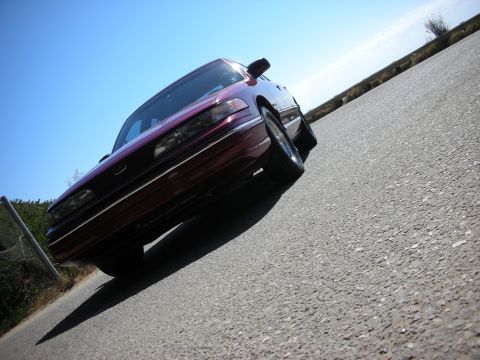 1992 Ford Crown Victoria - A maroon sedan is parked on a road under a clear blue sky.