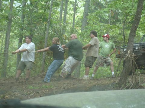 1996 Ford Bronco - Five men pull on a winch cable attached to an off-road vehicle in a forest clearing.