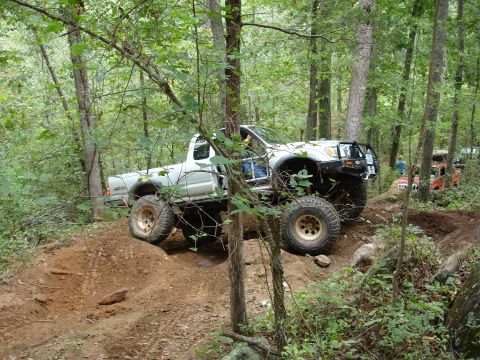 1996 Ford Bronco - A white pickup truck tackles a challenging off-road course, with other vehicles visible in the background.