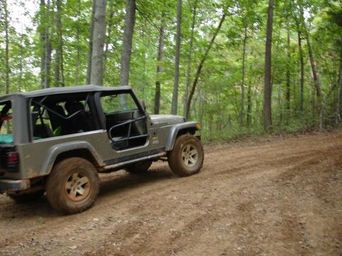 1996 Ford Bronco - A gray Jeep Wrangler navigates a dirt path through a wooded area.