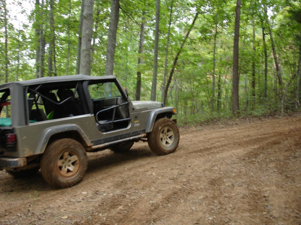 Gray Jeep Wrangler with aftermarket doors and roll cage on a dirt road