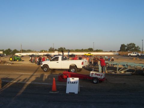 1994 Ford F-150 - A white pickup truck with prominent dual exhaust stacks is positioned at a truck pull event, with spectators and other vehicles present.