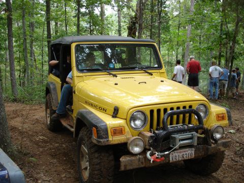 1996 Ford Bronco - Yellow Jeep Wrangler Rubicon on a wooded trail with several people watching.