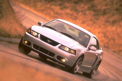 2003 Ford Mustang - A silver 2003 Ford Mustang is captured in a three-quarter front view as it drives along a dusty road.