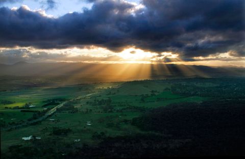 2000 Ford Crown Victoria - Dramatic sunbeams pierce the clouds, illuminating a vast rural landscape at dusk.