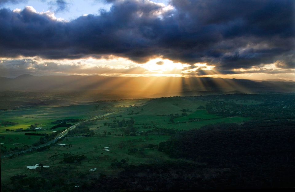Sun rays breaking through storm clouds over a green valley with a winding highway