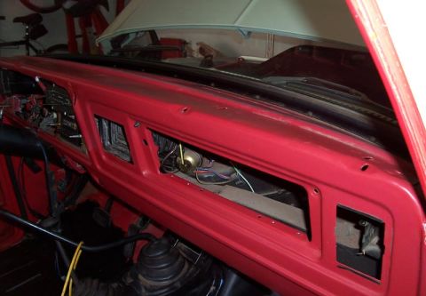 1978 Ford Bronco - The interior of a vehicle shows a red dashboard with exposed wiring and vents, with the hood open.