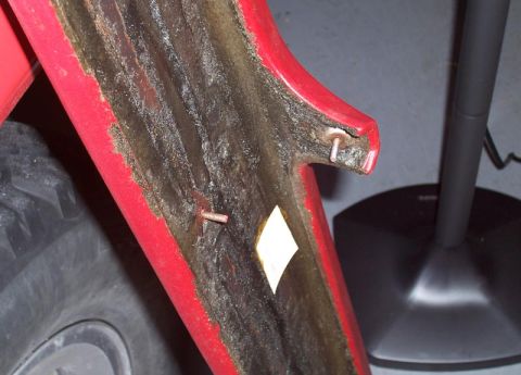1978 Ford Bronco - Close-up of a red fender liner interior showing damage and exposed materials, with a yellow sticker attached.