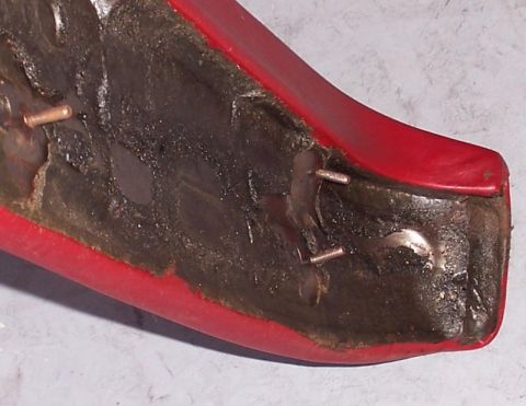 1978 Ford Bronco - Close-up view of a red car interior part, showing exposed copper pins and dark padding material.