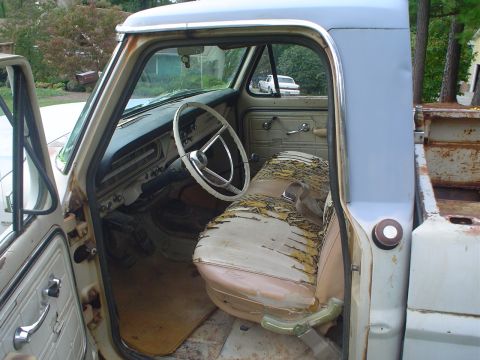 1967 Ford F-250 - The interior of a vintage pickup truck, a worn seat and dashboard, with another vehicle visible in the background.