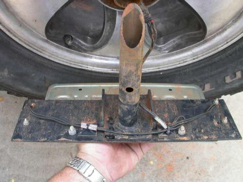 1990 Ford Bronco - A trailer hitch mount with wiring is held by a hand near a tire, showing part of the vehicle's rear.