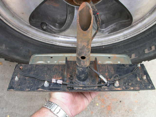 Trailer hitch mount with wiring, held by a hand with a watch, near a tire