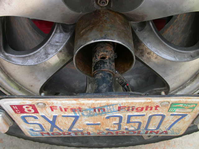 Close-up of a rusty exhaust pipe and a North Carolina license plate reading SXZ 3507